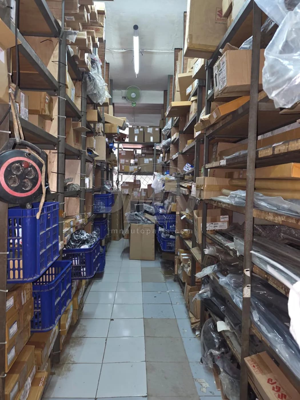 Aisle of floor-to-ceiling shelving holding boxed Suzuki spare parts at the JMN Jakarta warehouse
